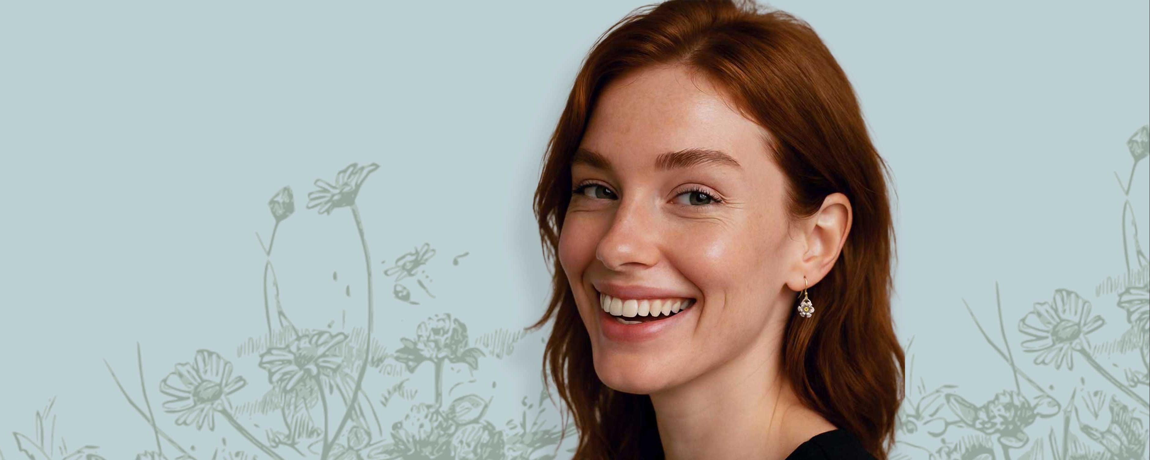 Smiling woman with red hair wearing Blossom silver and yellow sapphire drop earrings against a light blue background with subtle floral patterns.