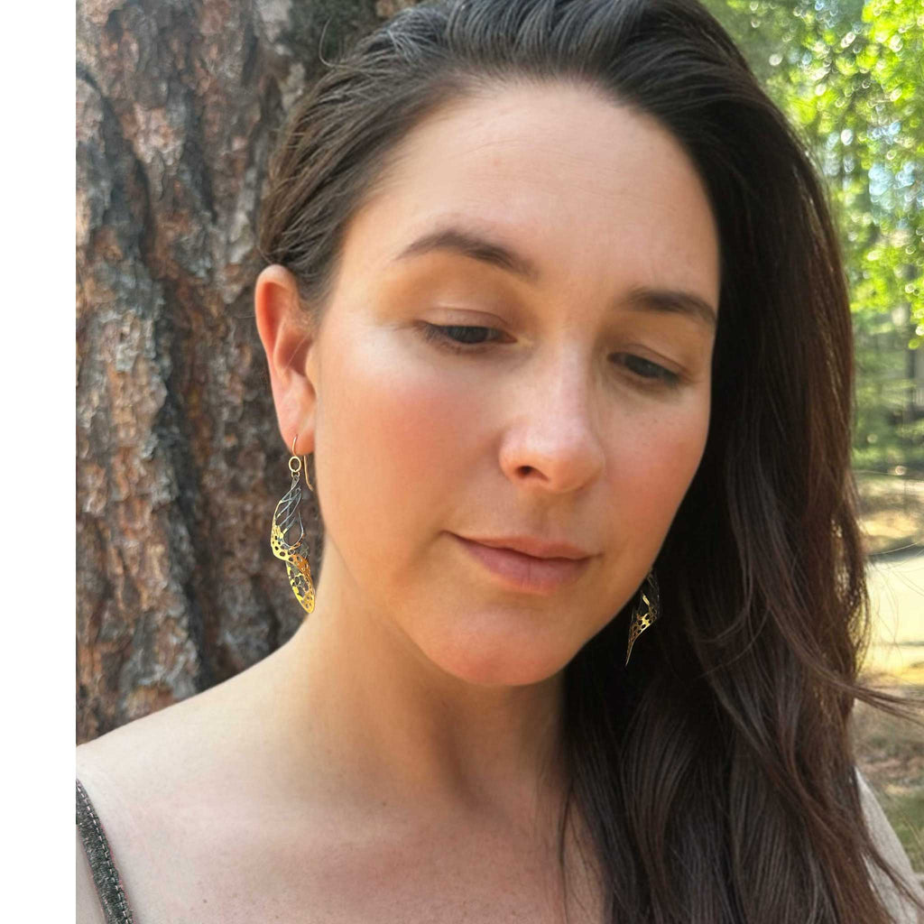 Woman with long dark hair and Chrysalis keum-boo butterfly earrings standing outdoors with a tree in the background
