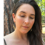 Woman with long dark hair and Chrysalis keum-boo butterfly earrings standing outdoors with a tree in the background