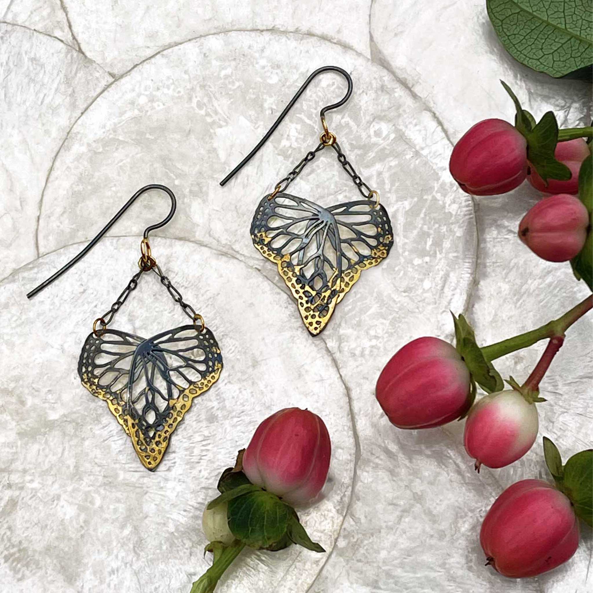 Butterfly-shaped earrings on a textured surface with pink flowers.