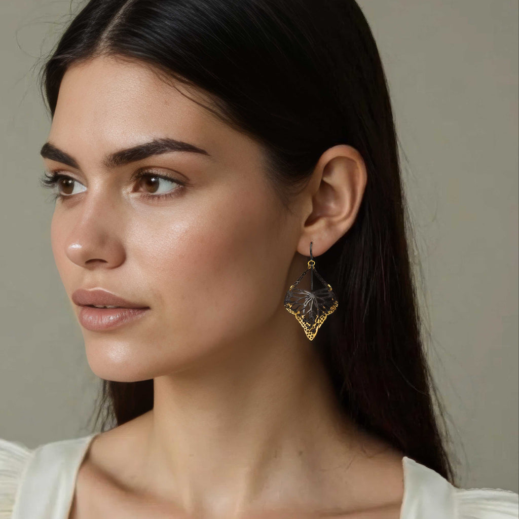 Woman wearing gold and oxidized silver Flutter monarch earrings with a neutral background