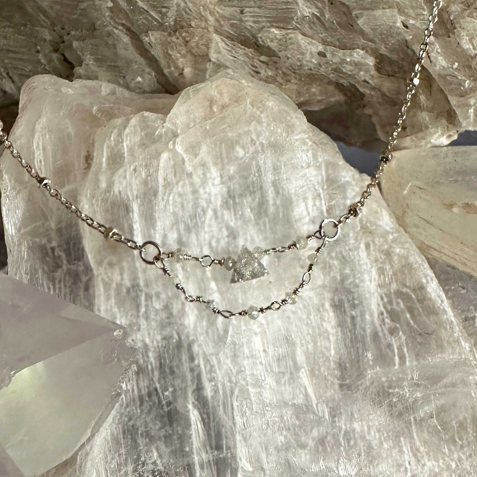 Grey Dawn raw triangle diamond necklace draped over a crystal formation