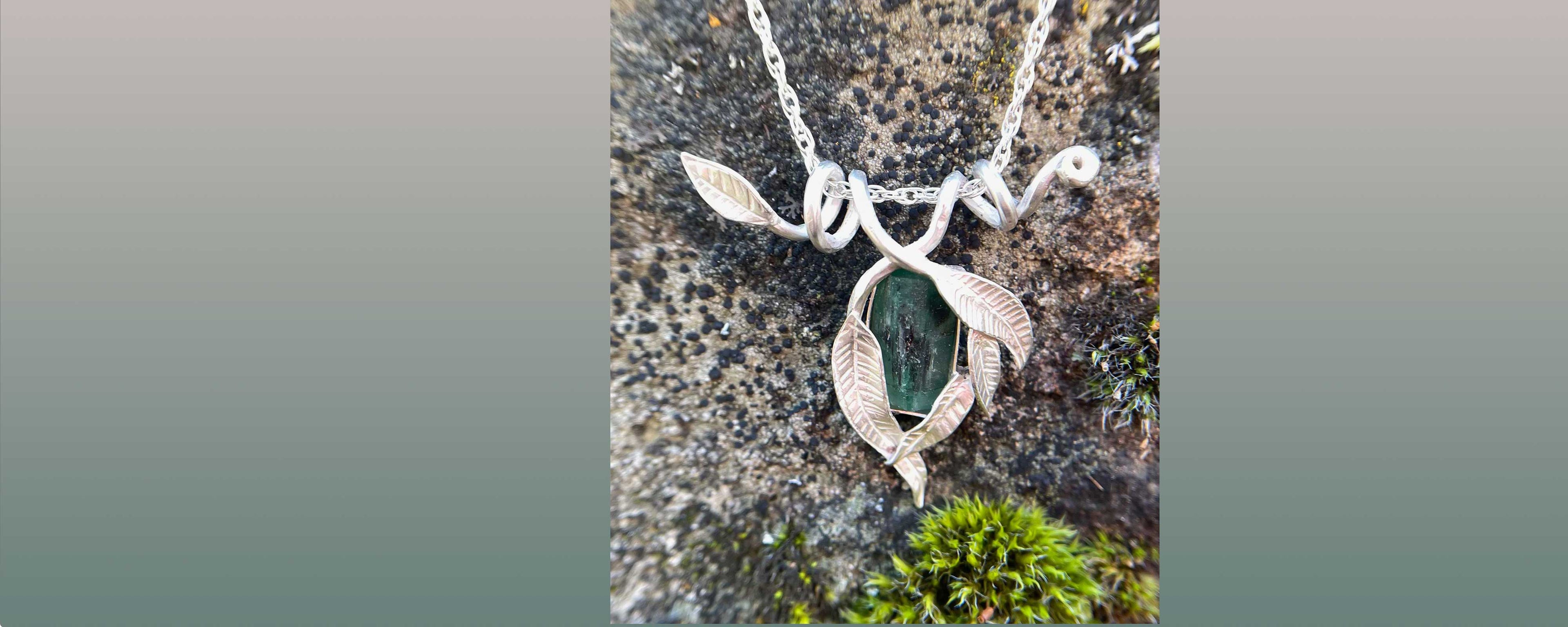Emerald necklace framed in silver leaves on a textured stone background