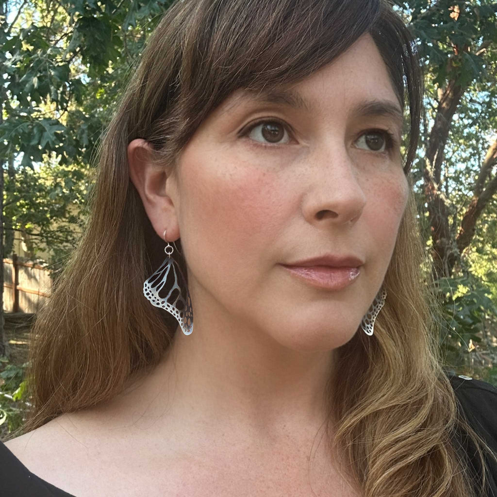 Woman with Monarch butterfly black and silver earrings with trees in the background