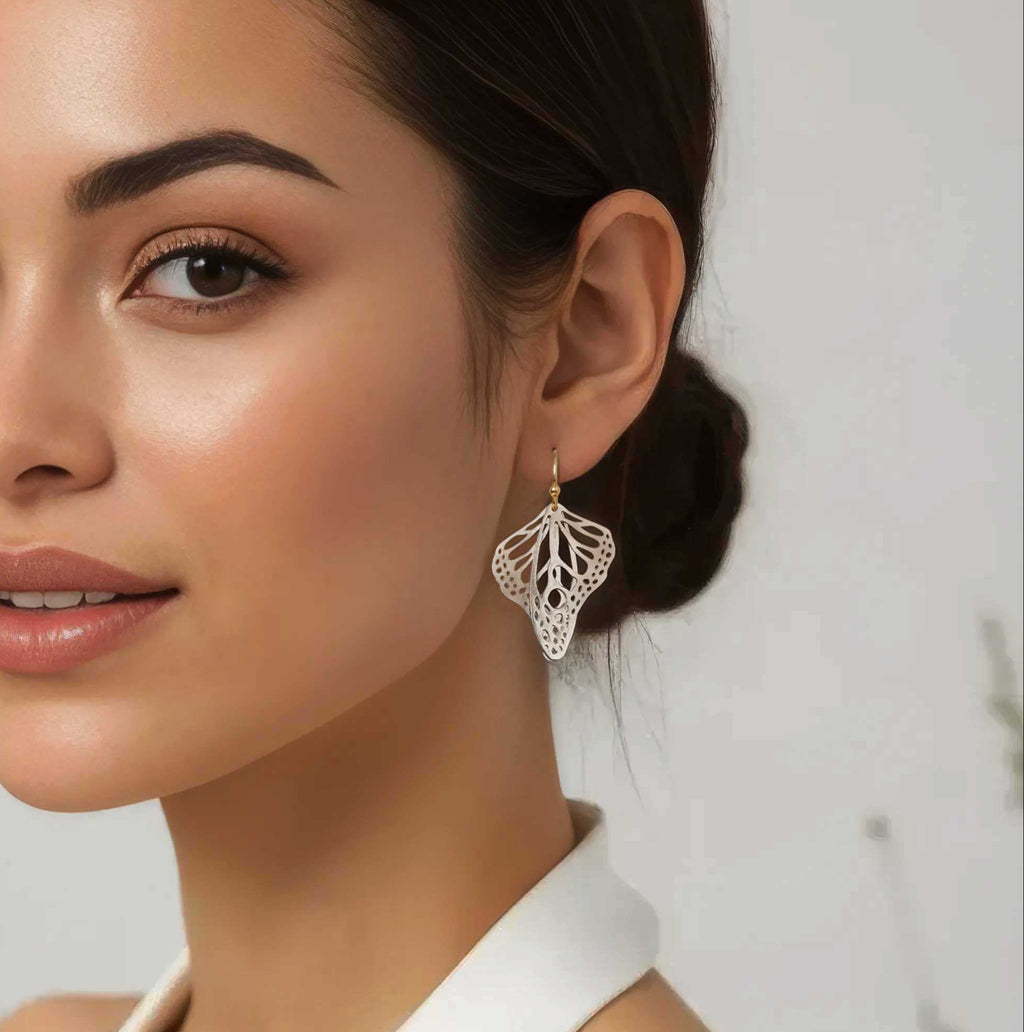 Woman wearing silver handmade butterfly wing earrings with 14k gold ear wires over a blurred background | Camille Torres Designs