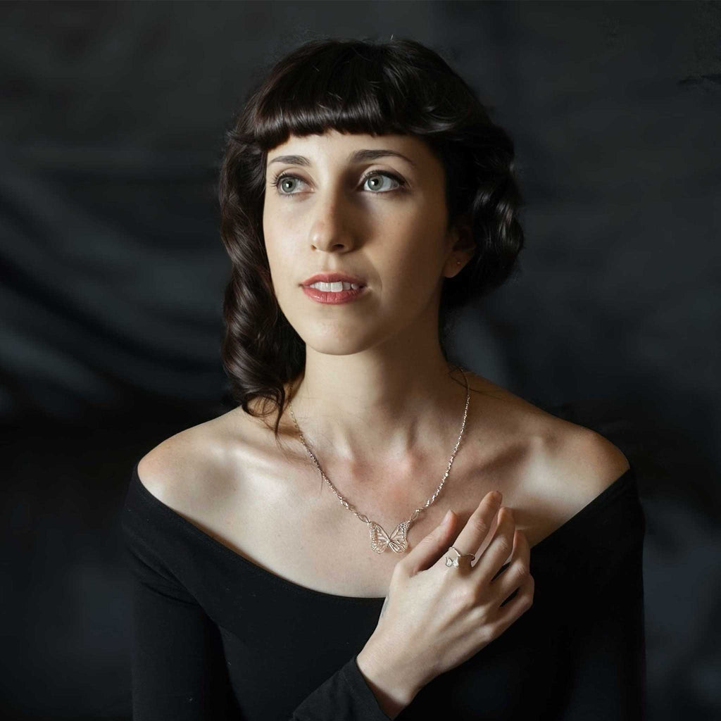 Woman wearing a silver Migration butterfly necklace and ring against a dark background