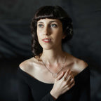 Woman wearing a silver Migration butterfly necklace and ring against a dark background