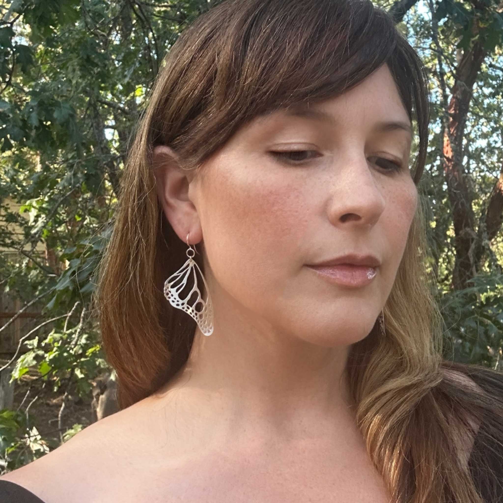 Camille wearing a silver Monarch earring with a natural background