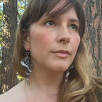 Woman wearing large, intricate oxidized silver Overwinter monarch butterfly earrings with a natural background