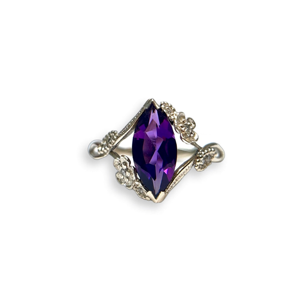 Front view of custom floral engagement ring with a purple colored marquise gem in white gold and diamond accents over a white background | Camille Torres Designs