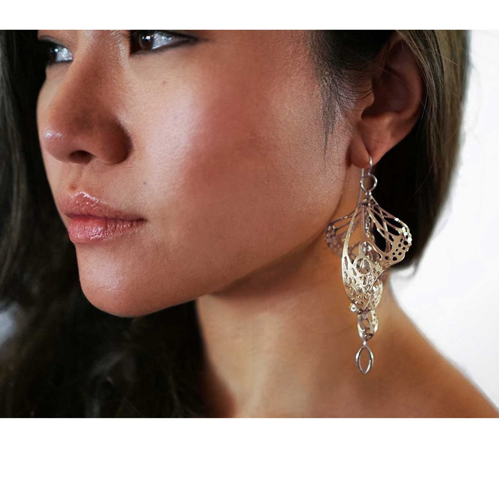 Close-up of a woman wearing a silver Overwinter chandelier butterfly earring with a white background