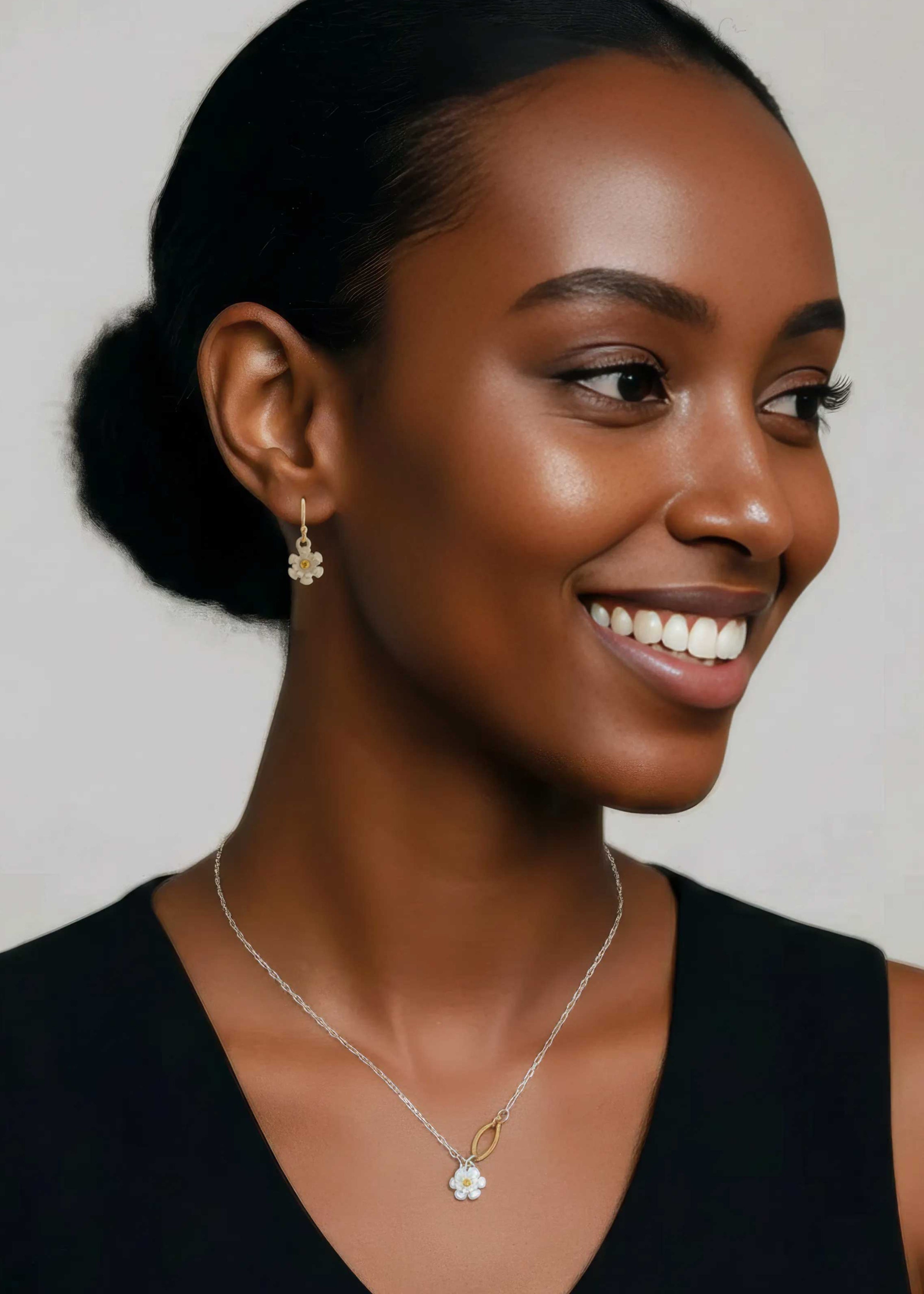 Woman wearing Blossom mixed metal silver charm necklace and drop earrings with yellow sapphire centers and 14k gold accents on a neutral background | Camille Torres Designs