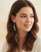 Woman wearing Chrysalis silver drop butterfly earrings and a white blouse with a blurred background