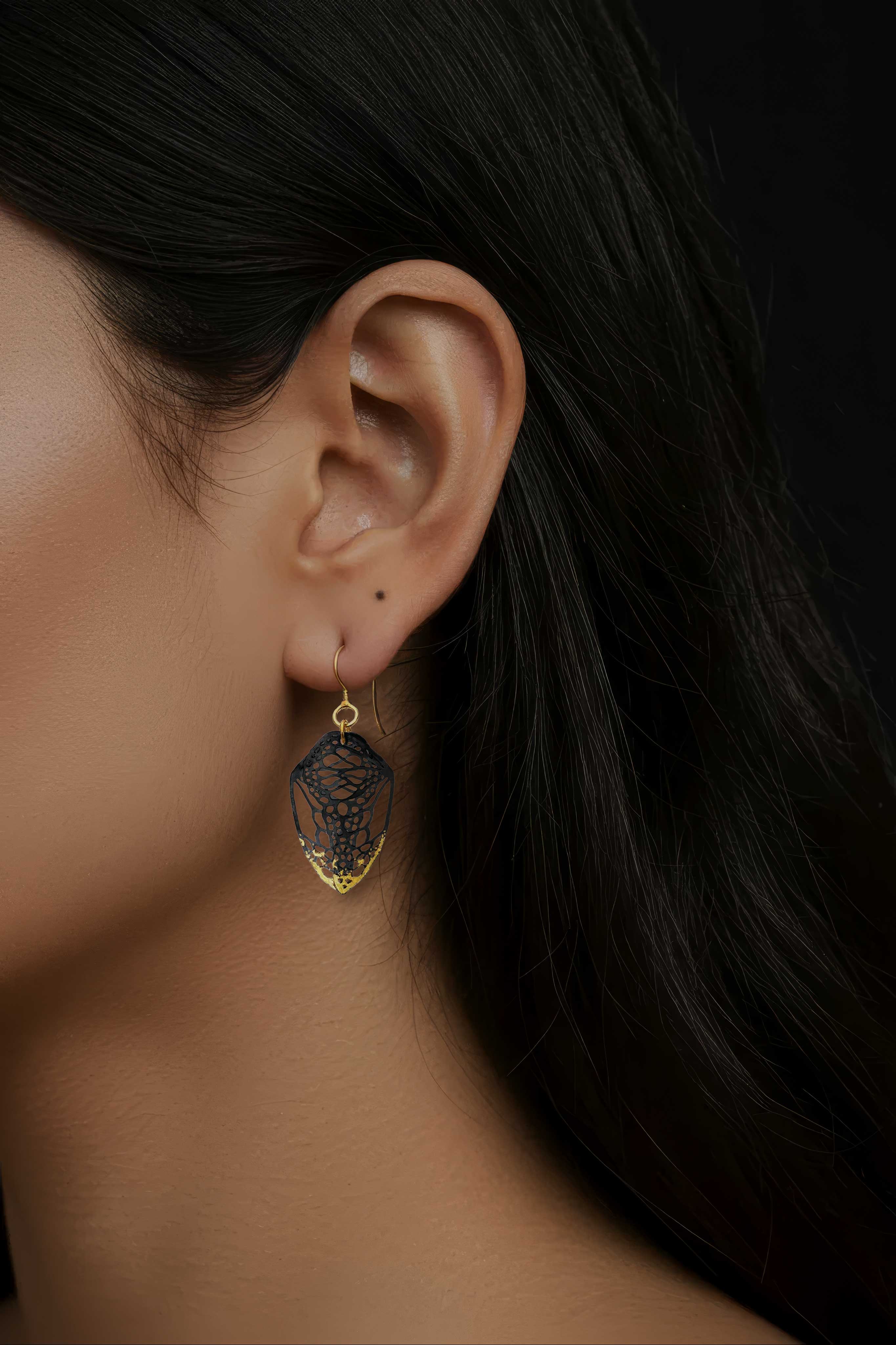 Close-up of an ear wearing handcrafted mixed metal 24k gold and patina silver Cocoon butterfly earrings with dark hair in the background | Camille Torres Designs