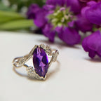Custom colored stone engagement ring with a purple gem in  floral vines in 18k white gold in front of purple flowers | Camille Torres Designs