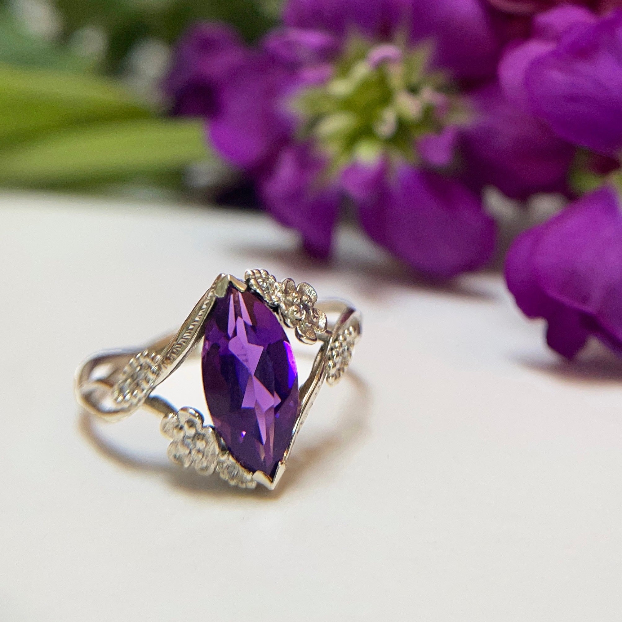 Custom colored stone engagement ring with a purple gem in  floral vines in 18k white gold in front of purple flowers | Camille Torres Designs