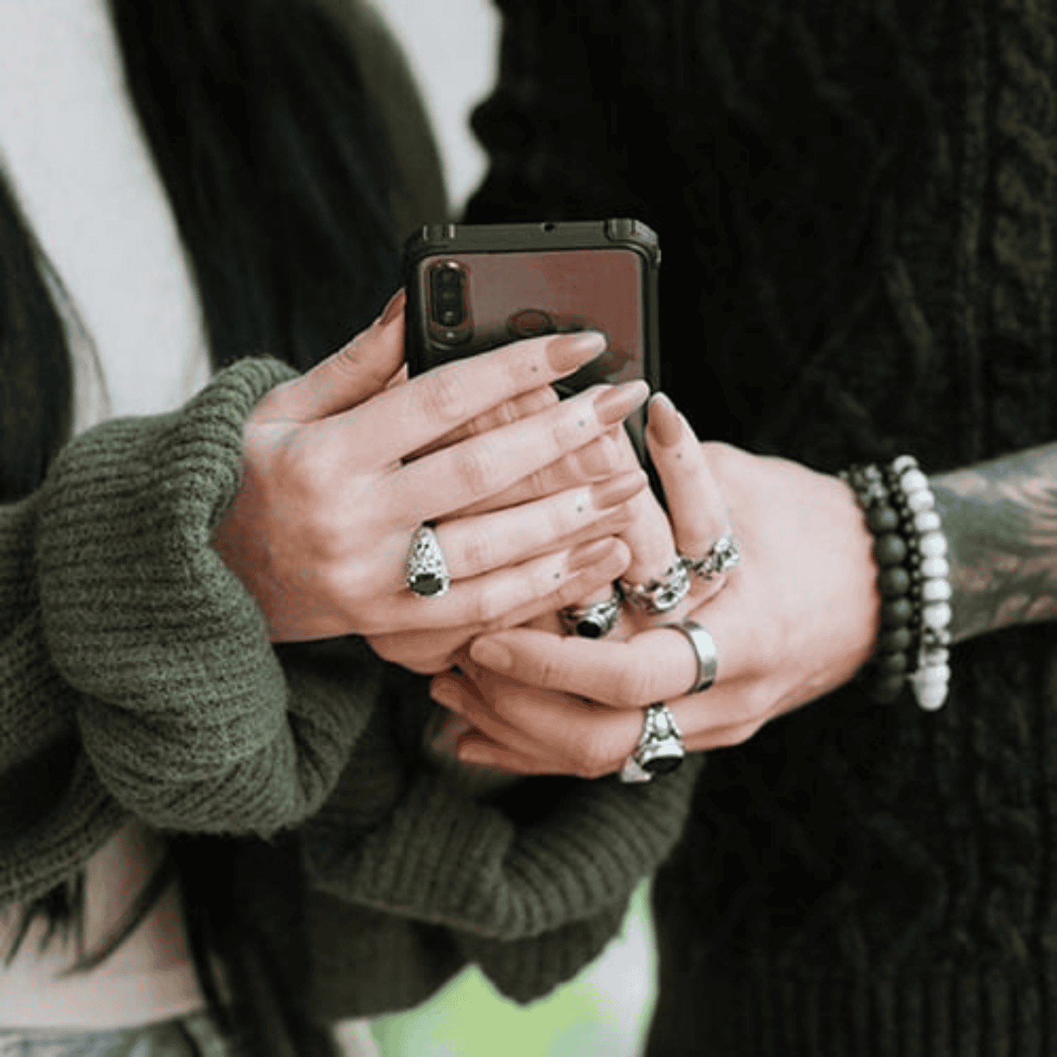 Two people holding a smartphone with close-up of hands and rings.