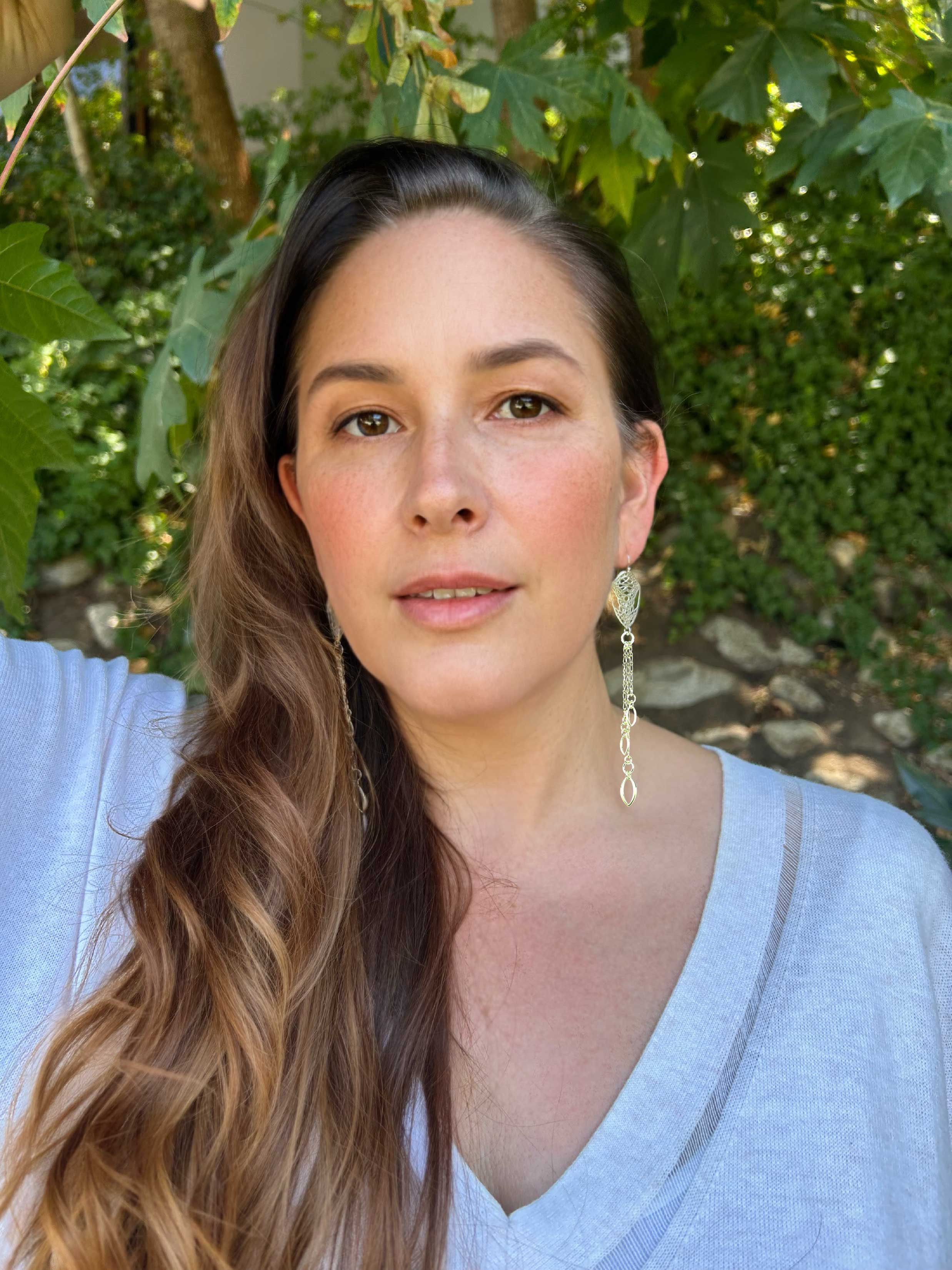Camille with long hair and butterfly cocoon chandelier earrings standing outdoors