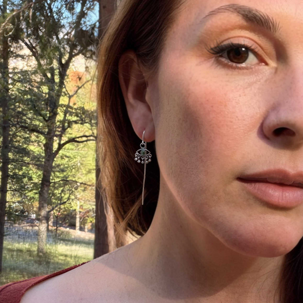 Sentinel evil eye silver threaders with green tourmaline up close on a model standing in front of trees | Camille Torres Designs