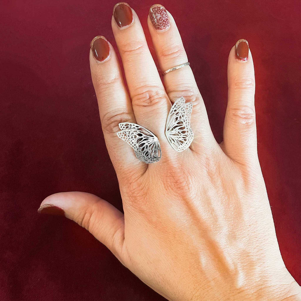 A hand wearing Flight silver butterfly-statement ring, set against a dark red background. | Camille Torres Designs