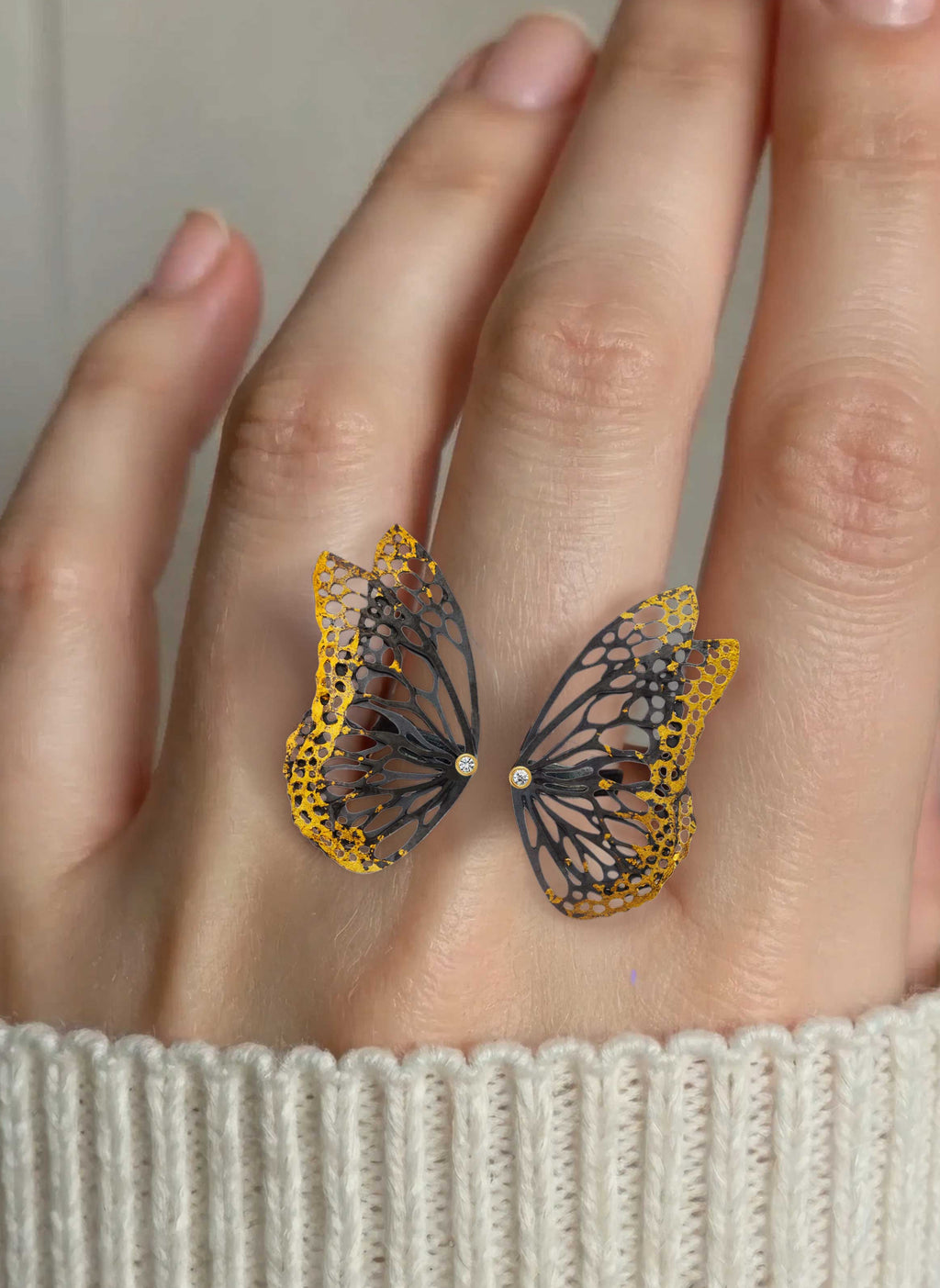 A close-up of a hand wearing Flight Keum-boo butterfly ring with diamond accents, styled with a cream ribbed knit sweater.