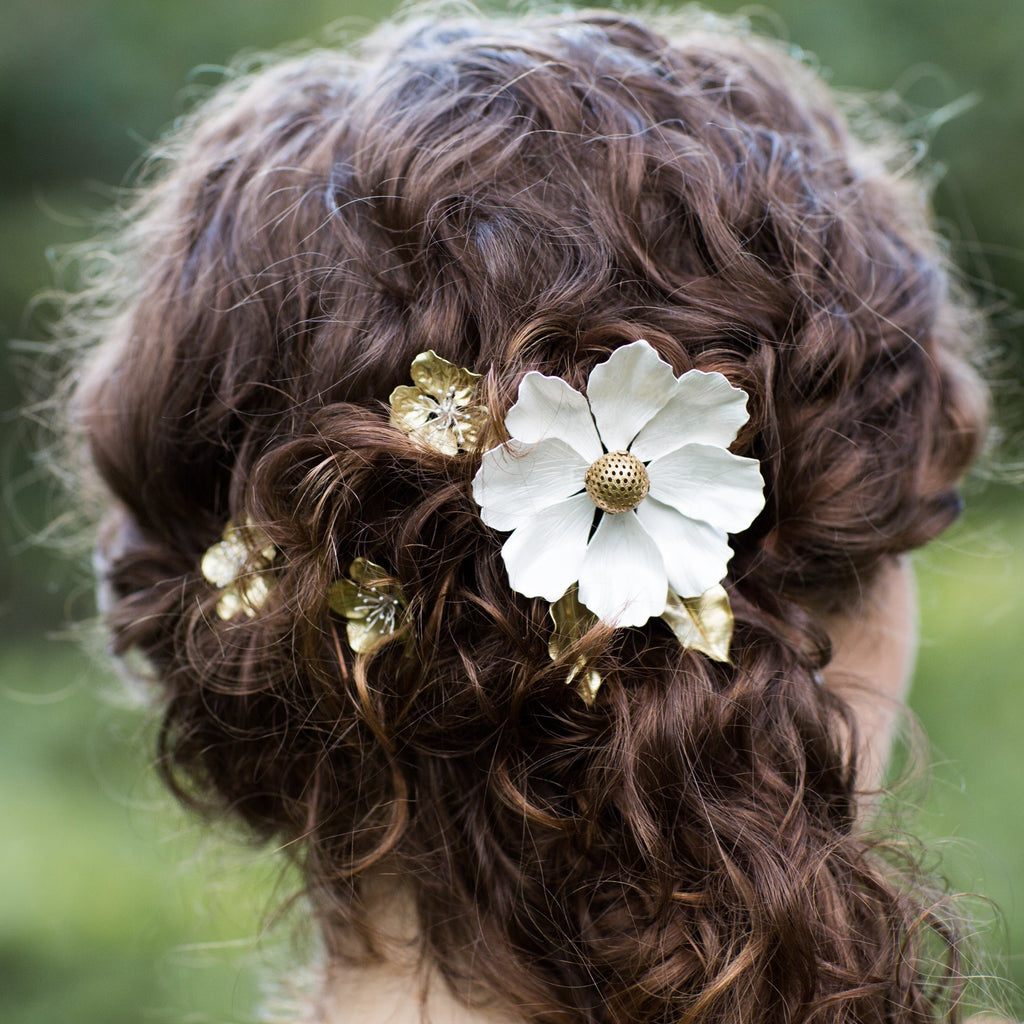 Bride with curly hair adorned with decorative custom floral hair combs against a blurred green background