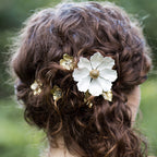 Bride with curly hair adorned with decorative custom floral hair combs against a blurred green background