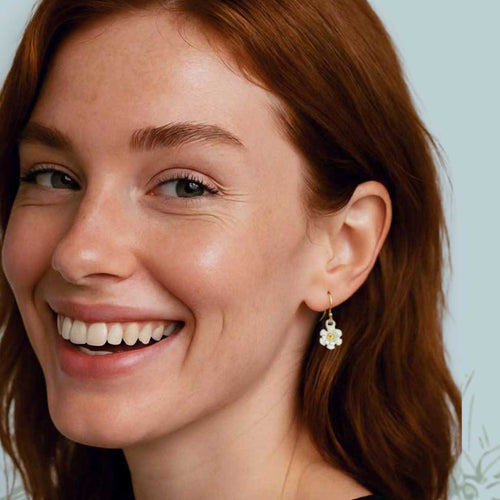 Young woman wearing Blossom drop earrings with yellow sapphire centers on a light blue background | Camille Torres Designs