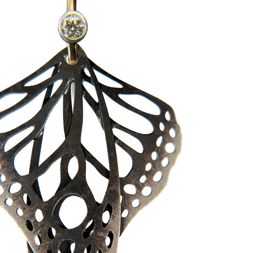 Close-up detail of Metamorphosis butterfly dangle earrings in oxidized silver with intricate lace wing pattern, 2 mm diamond with gold ear wires | Camille Torres Designs