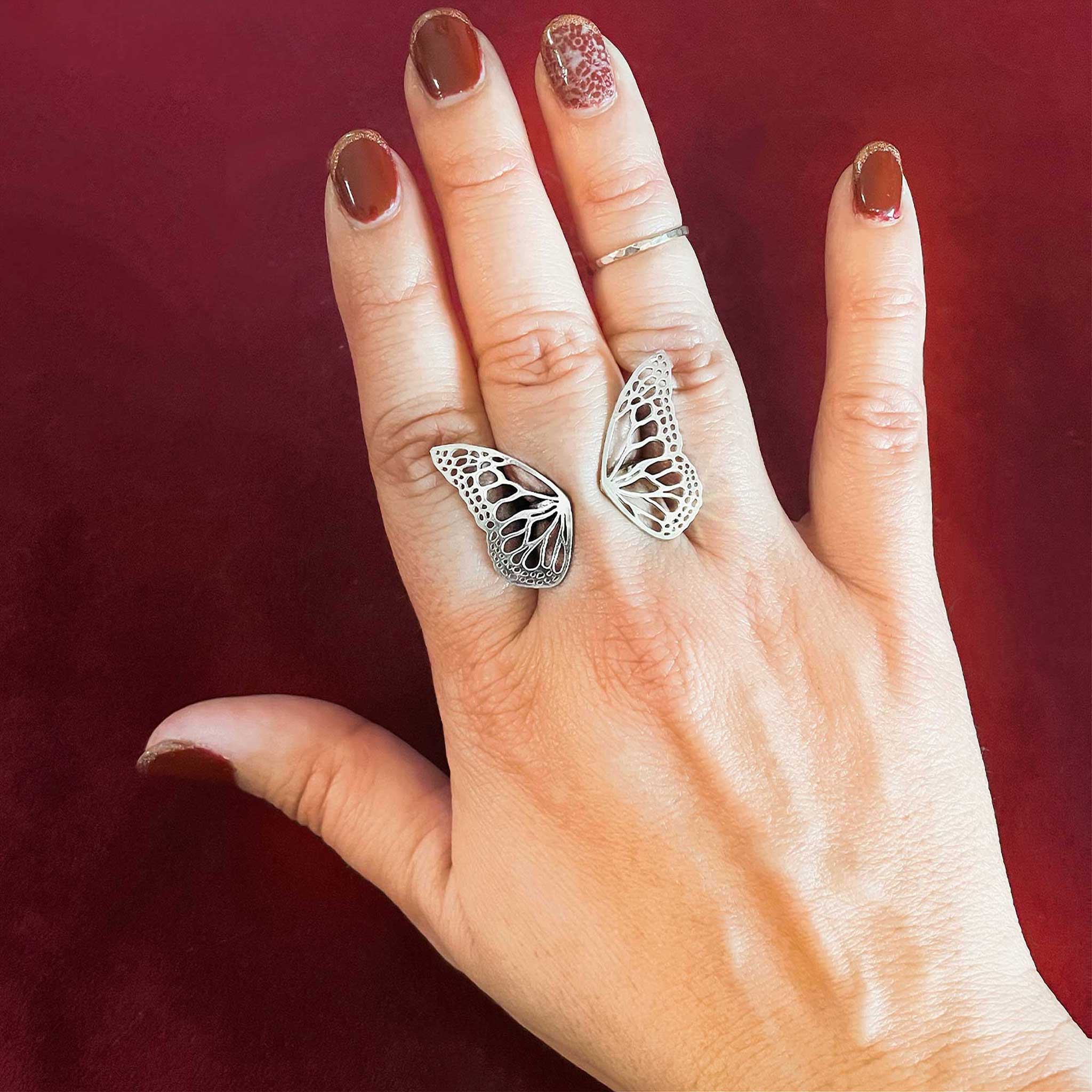 Migration adjustable silver butterfly ring worn on finger, showing dimensional wing wrap over a red background | Camille Torres Designs