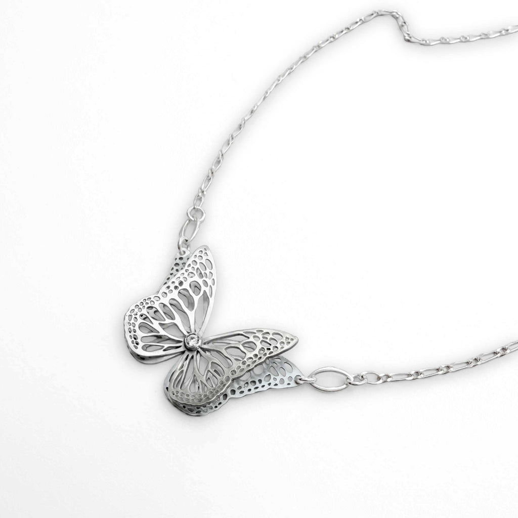 Side view of bright silver Migration butterfly necklace, showing overlapping wing detail and diamond on a white surface.