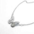 Side view of bright silver Migration butterfly necklace, showing overlapping wing detail and diamond on a white surface.