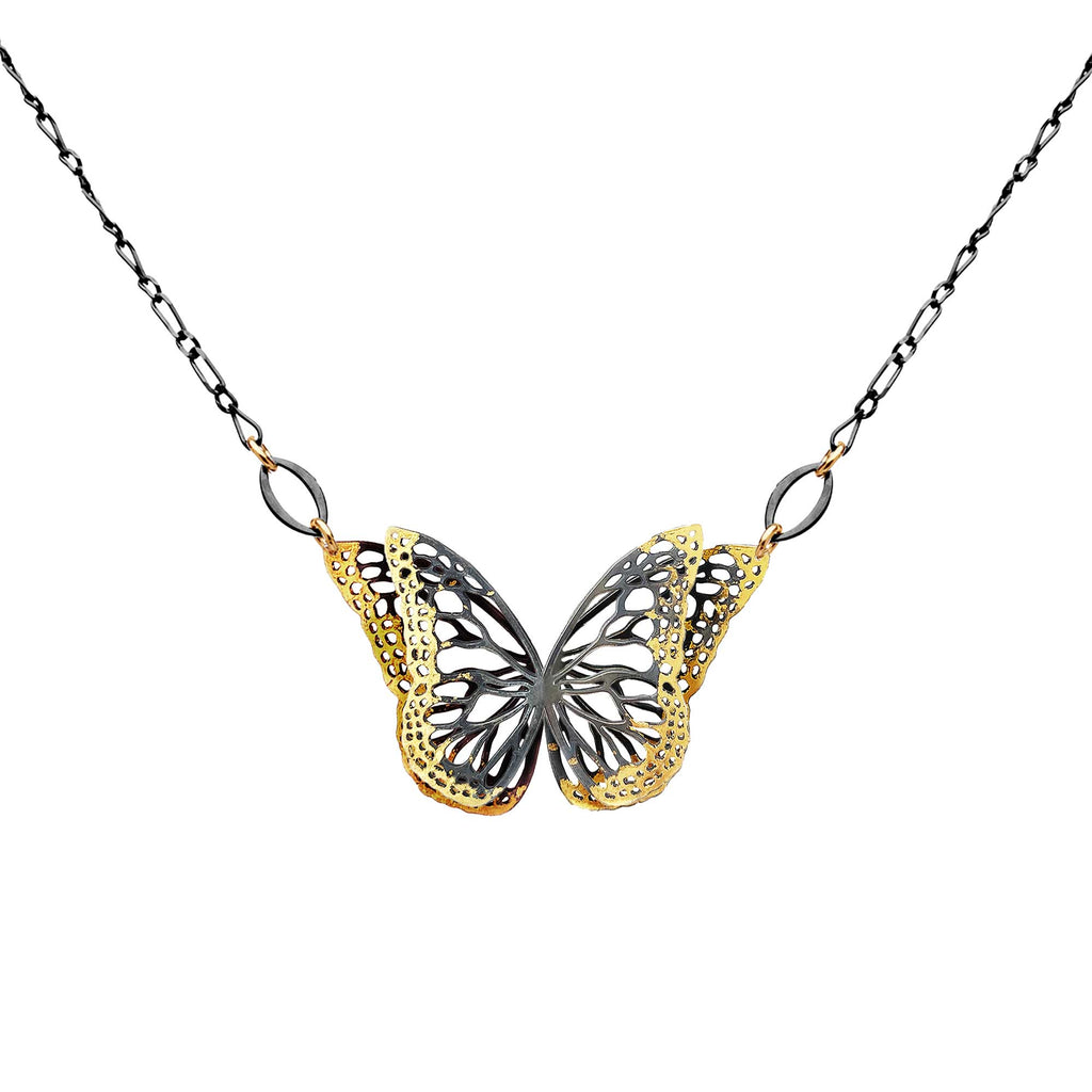 Migration, double winged butterfly pendant necklace with textured 24k gold and oxidized silver wings, suspended from a black silver chain on a white background.