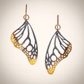 Monarch butterfly wing-shaped earrings with gold and silver gradient on a beige background