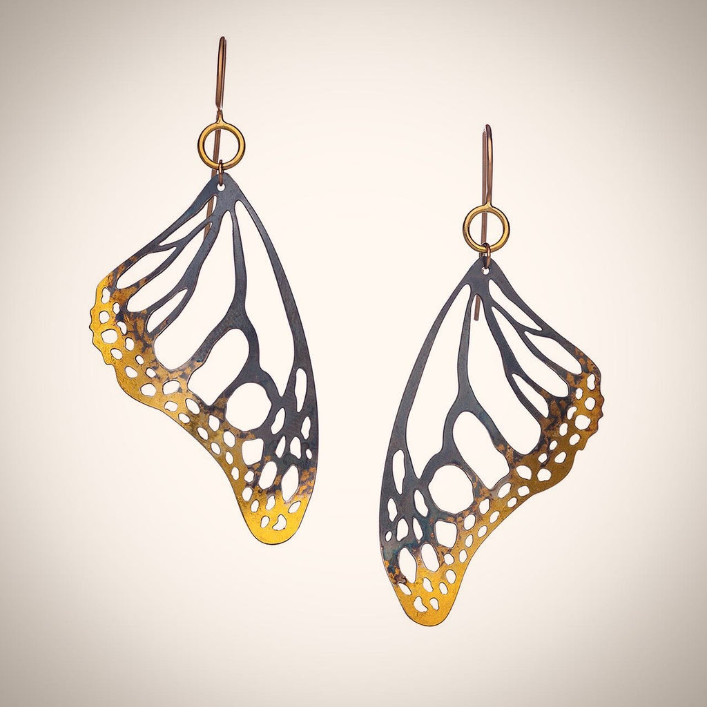Butterfly shaped earrings with 24k gold and black details on a white 