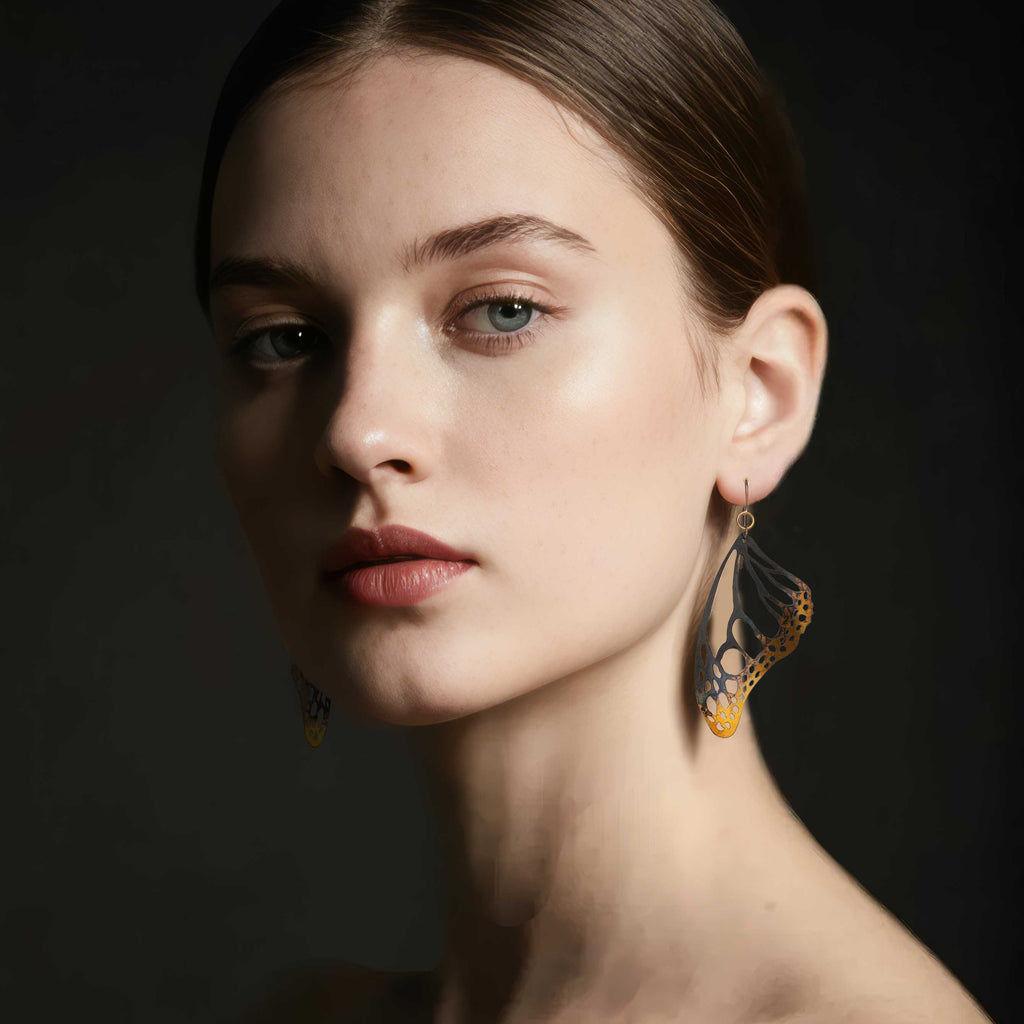 Woman wearing Monarch butterfly drop earrings with gold keum-boo silver against a dark background