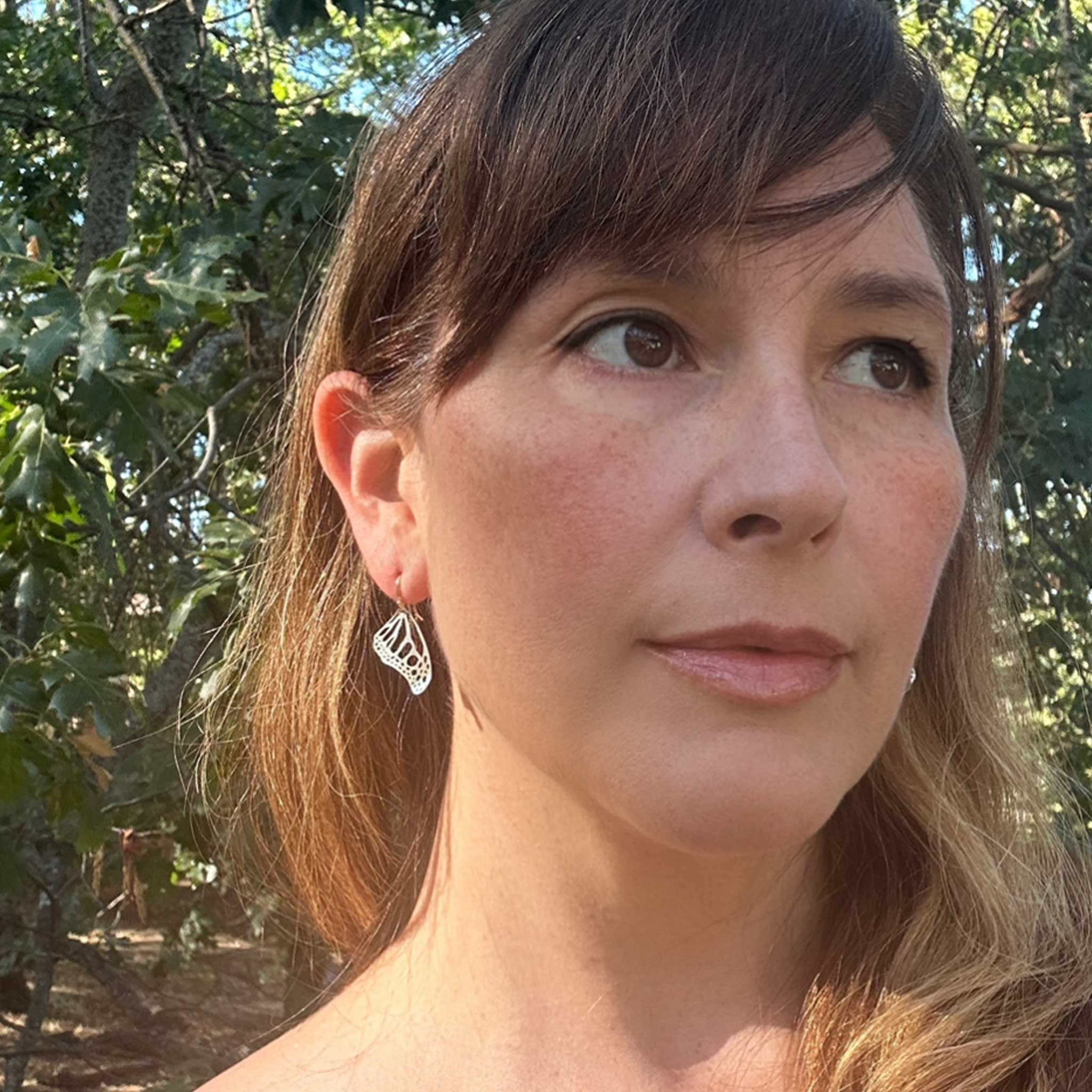 Camille with small Monarch wing earrings looking to the side with a natural background