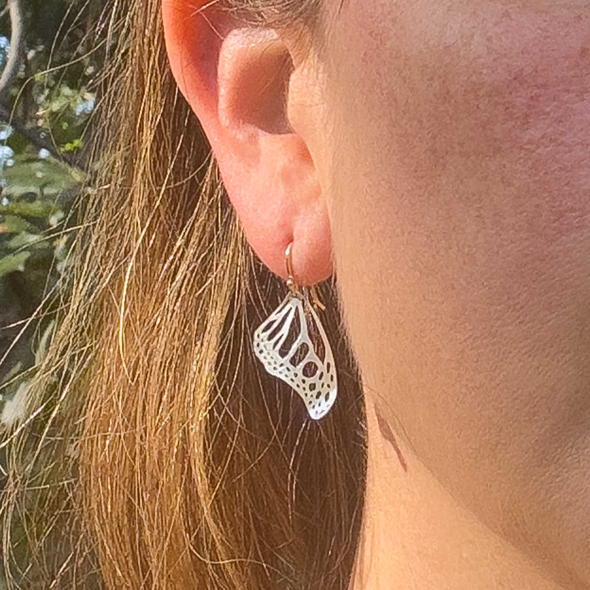 Close up of person wearing small Monarch butterfly dangle earrings in silver with 14k gold ear wires over a white background | Camille Torres Designs