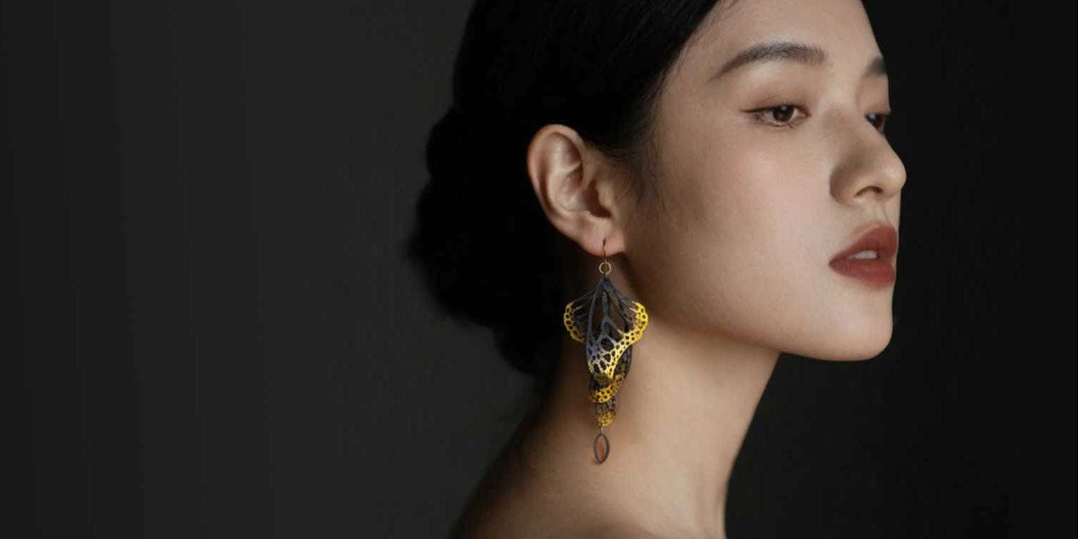 Woman wearing Overwinter butterfly chandelier earrings with gold against a dark background