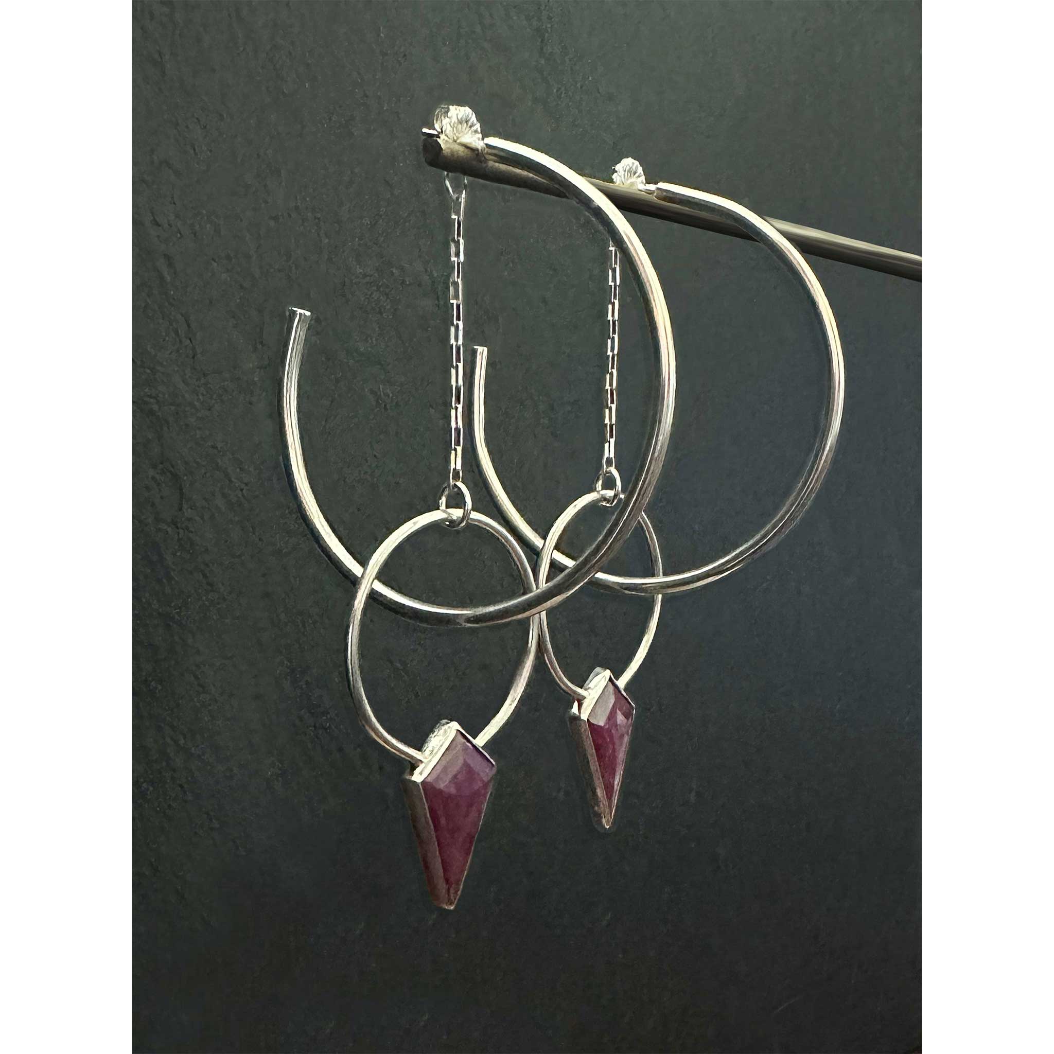 Side view of Ruby Halo Hoops showing dimensional layering of ruby jacket hoop behind 2-inch sterling silver hoop on dark background
