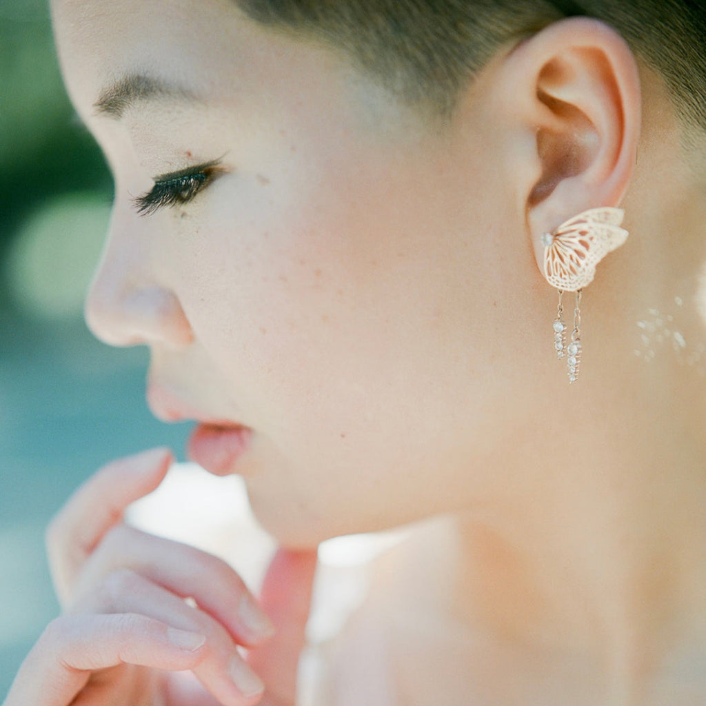 Bespoke bridal butterfly earring with rose gold and white sapphire in front os a blurred background | Camille Torres Designs