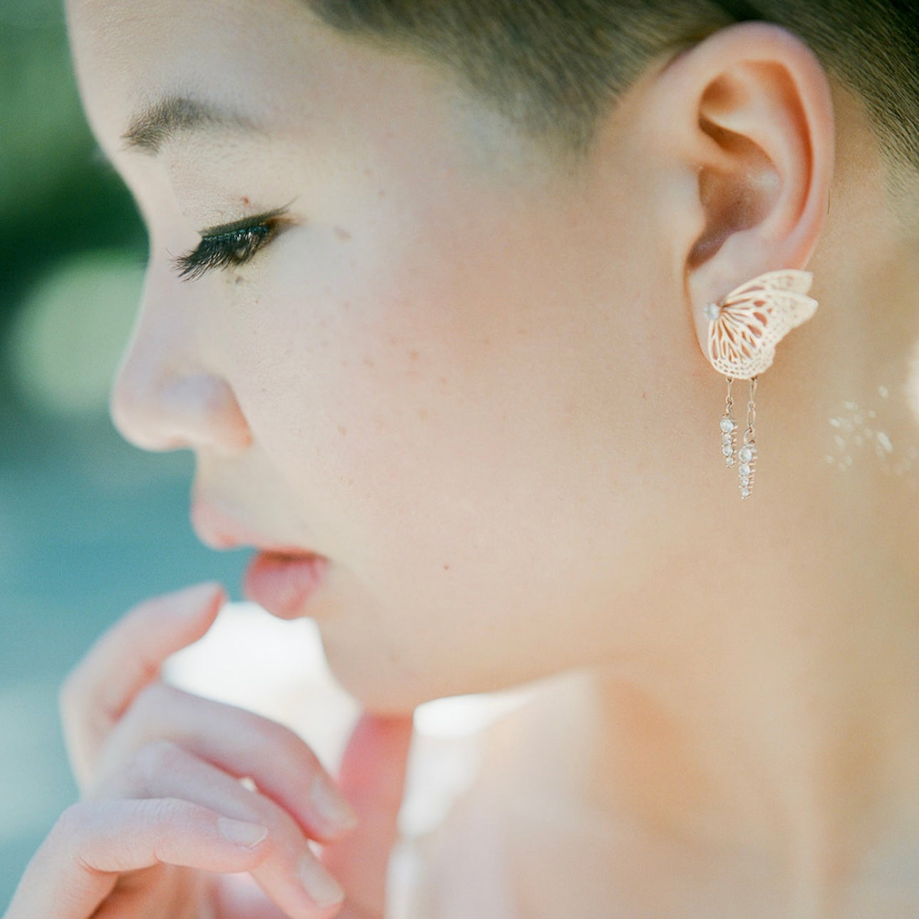 Bespoke bridal butterfly earring with rose gold and white sapphire in front os a blurred background | Camille Torres Designs