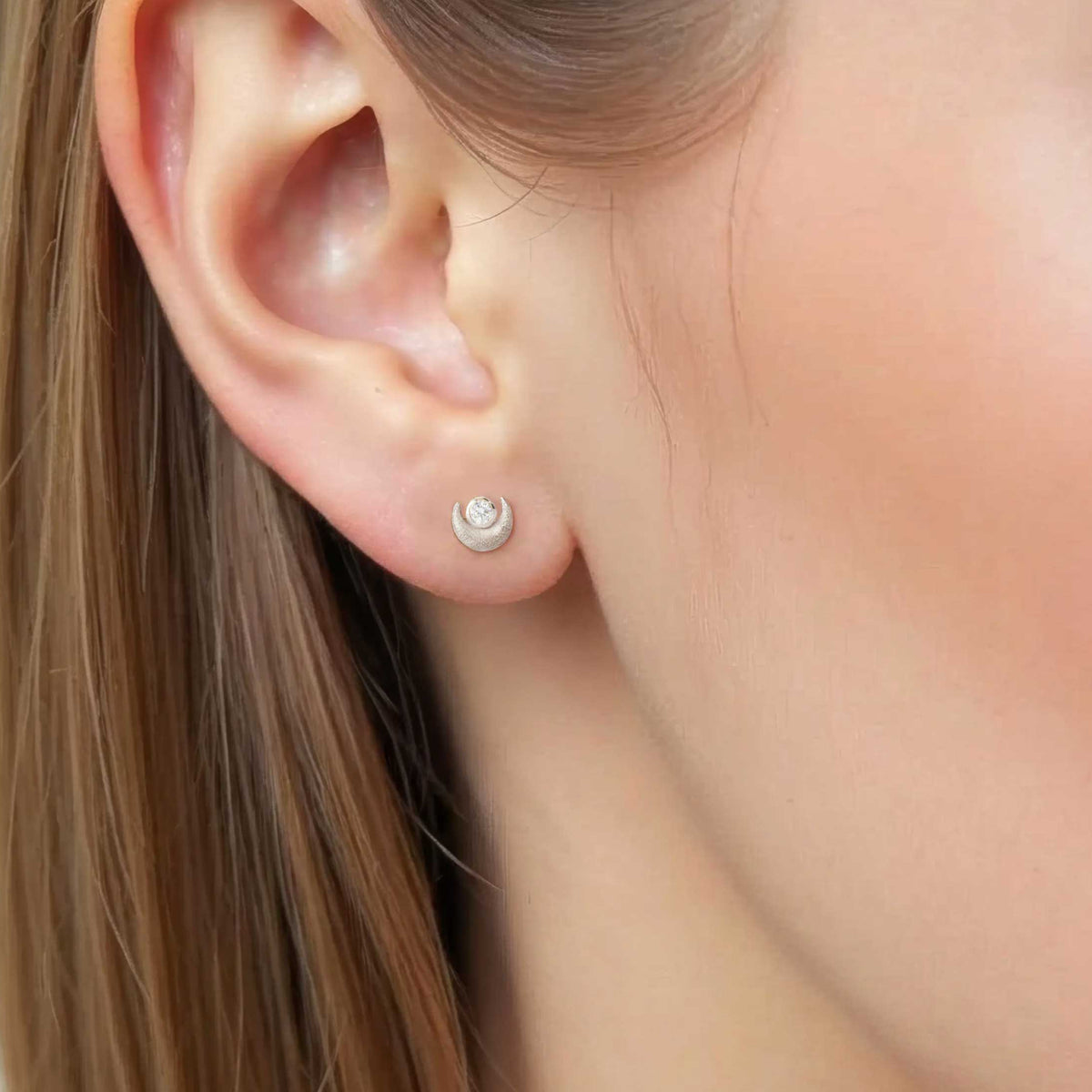 Cloesup of a woman wearing crescent moon silver stud with a brilliant white diamond on the dark side of the moon. Camille Torres Designs