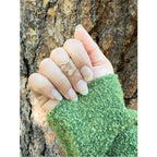 Hand wearing a silver Whisper butterfly charm ring with v-shaped band. A green textured sweater covers the wrist over a tree trunk | Camille Torres Designs
