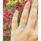 Hand wearing a silver hand crafted butterfly charm ring on a chevron ring shank with pink flowers in the background | Camille Torres Designs