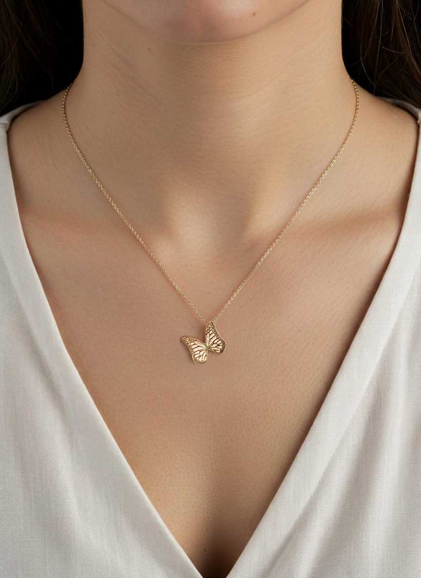 Gold Whisper necklace with a butterfly charm pendant worn by a person in a white top.