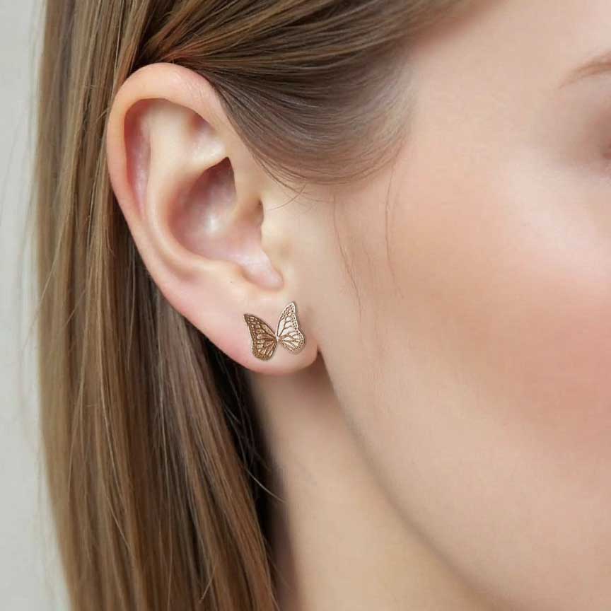 Gold Whisper butterfly earrings worn by a person with blond hair.