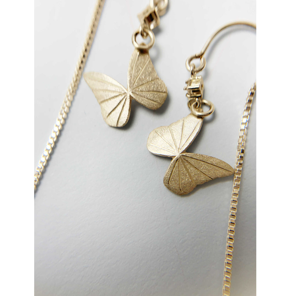 Back hand-engraving detail on 14k Gold butterfly threader earrings with diamonds on a white surface