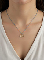 Gold Whisper necklace with a butterfly charm pendant on an oxidized silver chain worn by a person in a white top.