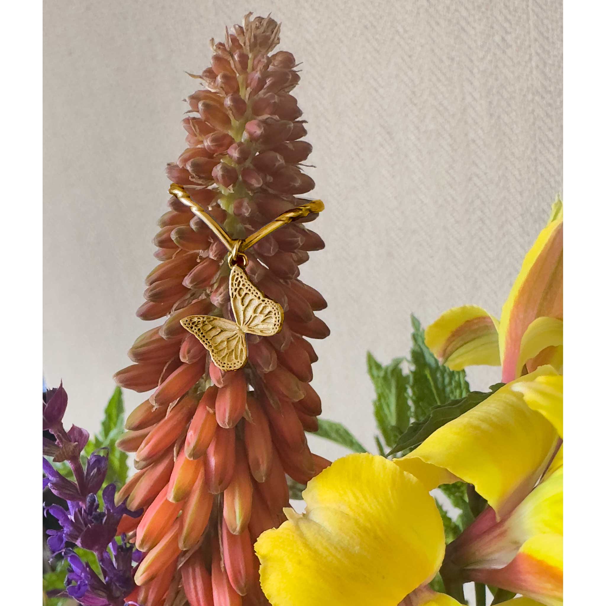Gold butterfly Whisper charm ring on a red flower with yellow flowers in the foreground